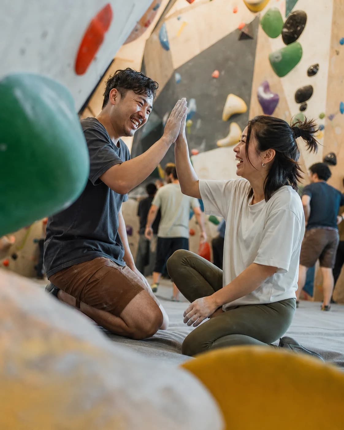 Illustrative Hong Kong bouldering scene with two adults sharing a high-five; not a member photo.